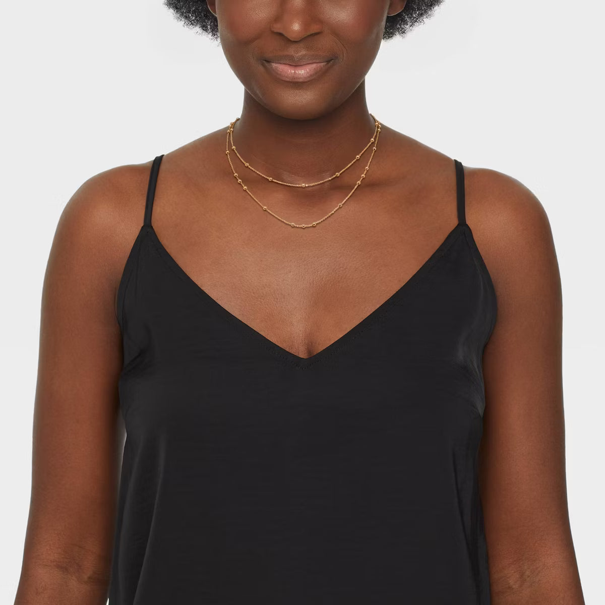 Woman wearing a black slip dress with gold necklaces on a white background