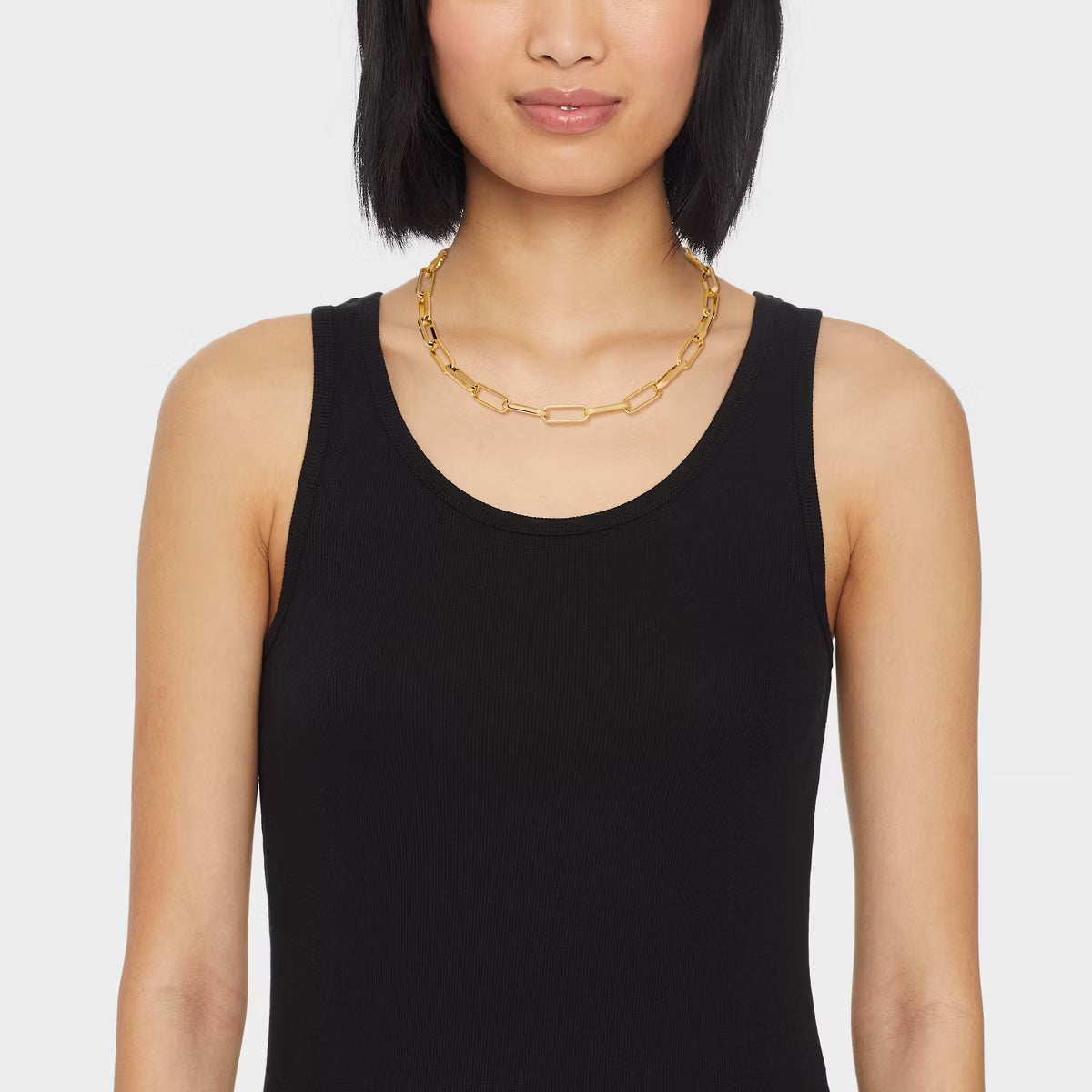 Woman wearing a black tank top and gold chain necklace on a white background