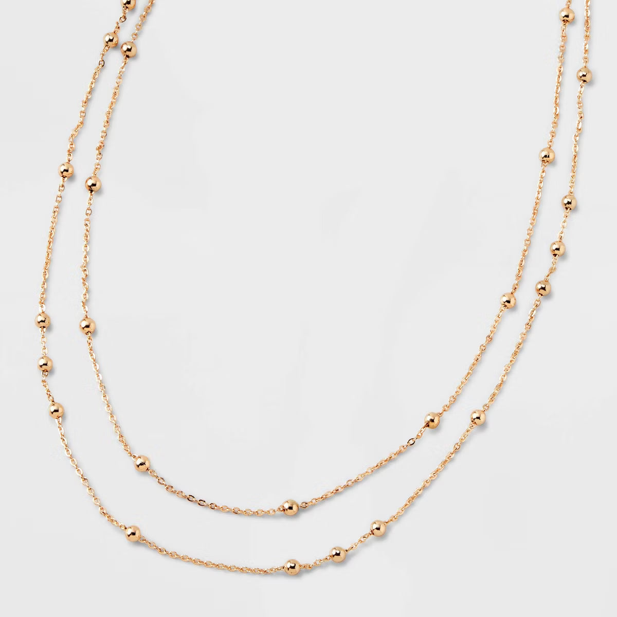 Two gold necklaces with small beads on a light gray background