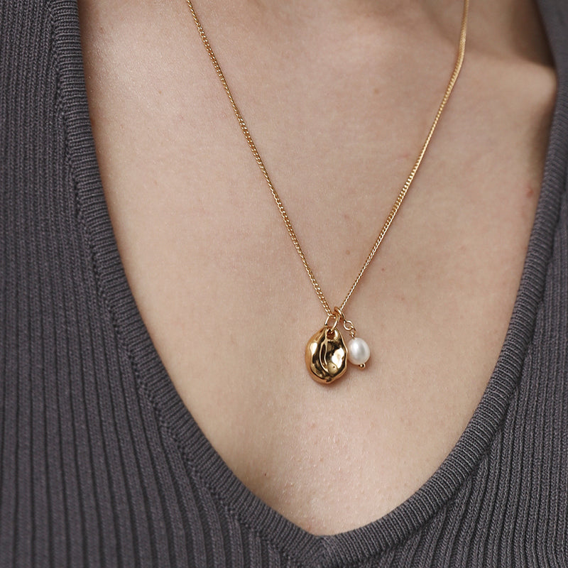 Gold necklace with a pearl pendant on a person wearing a gray top.
