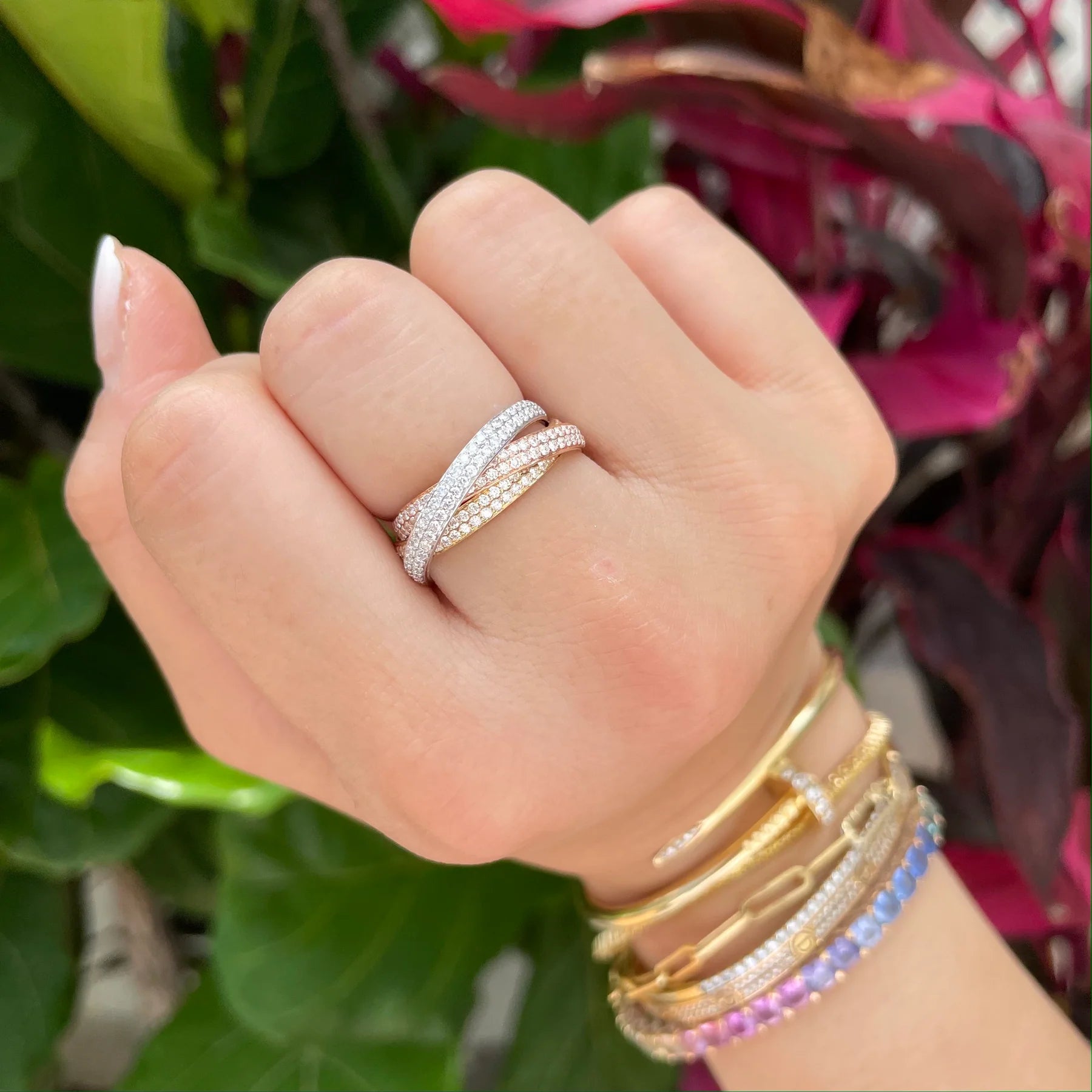 Hand wearing multiple rings and bracelets with a blurred floral background