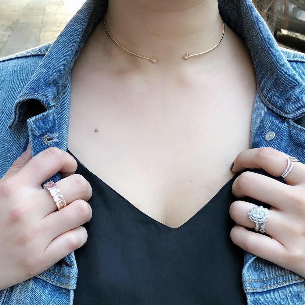 Person wearing a gold necklace, black top, and denim jacket with visible jewelry.