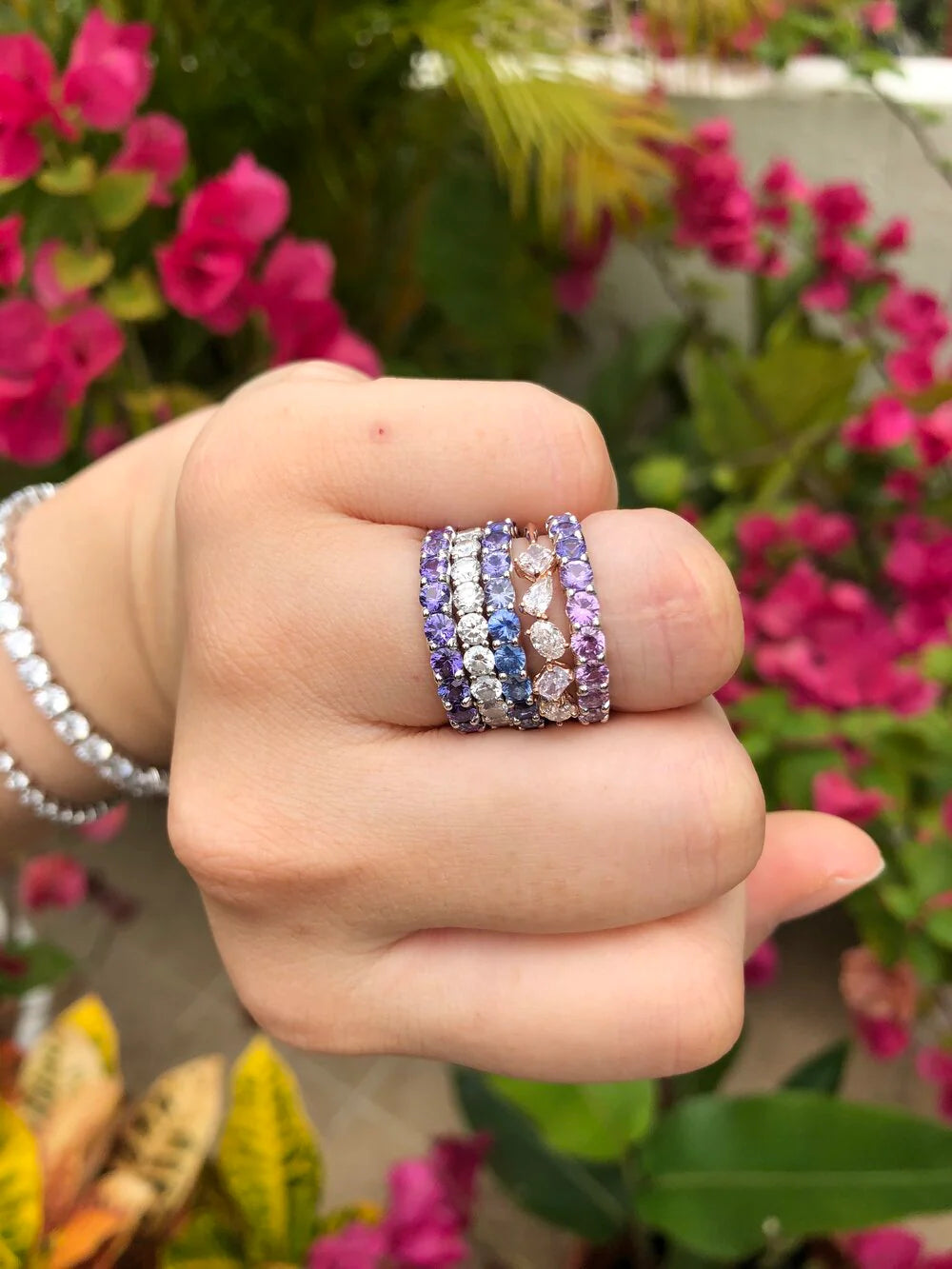Hand wearing multiple stackable rings with a floral background