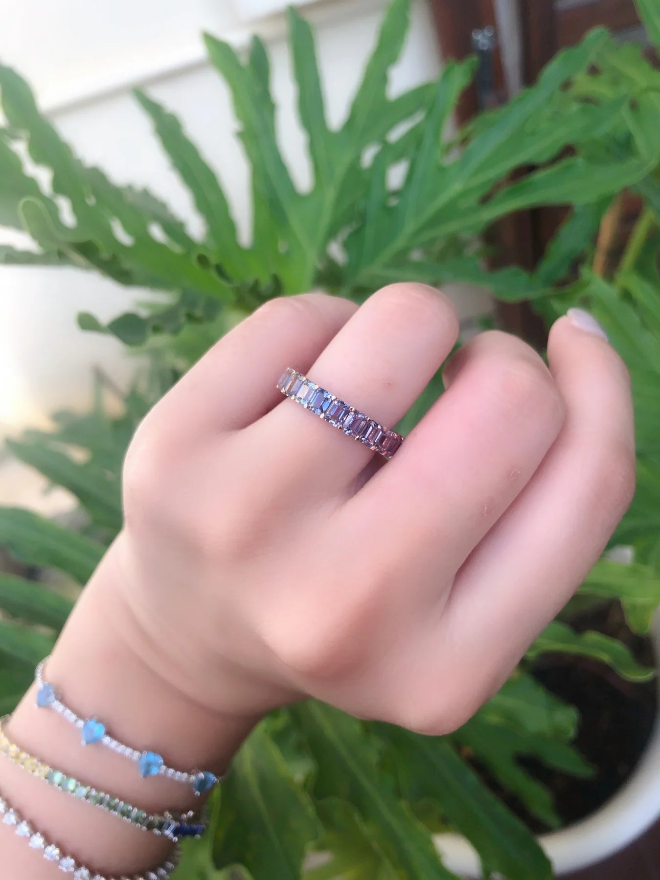 Hand wearing a ring with gemstones against a green leafy background