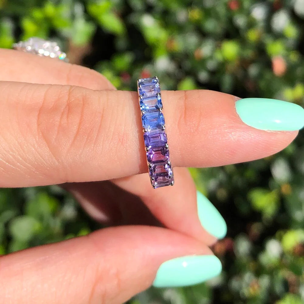 Emerald cut rainbow sapphire and diamond eternity ring on a hand