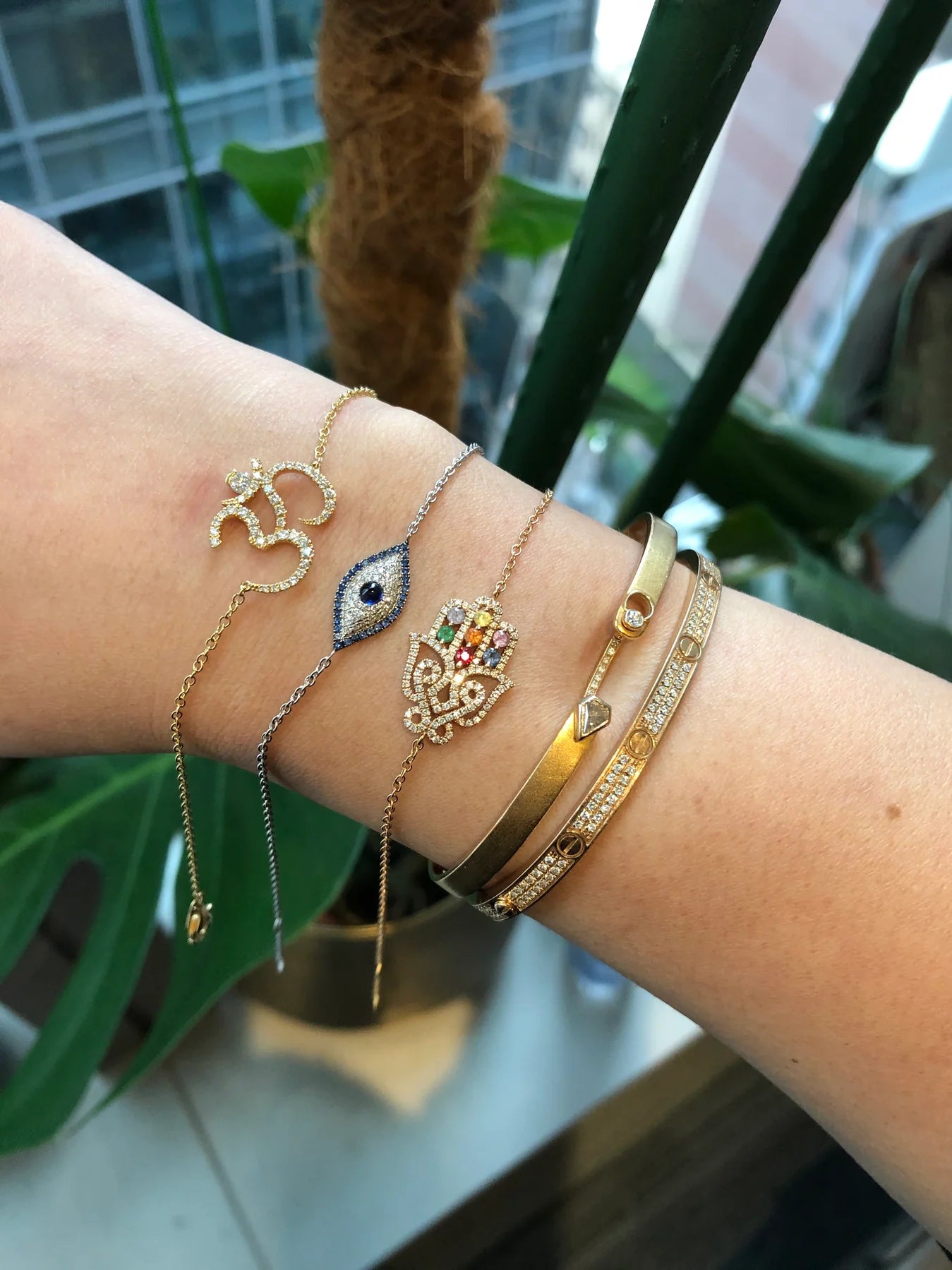 Wrist with multiple gold bracelets and rings against a blurred indoor background