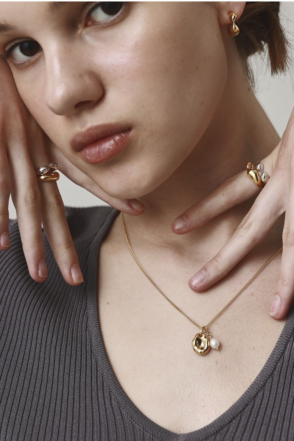 Close-up of a person wearing gold jewelry including a necklace, earrings, and rings.