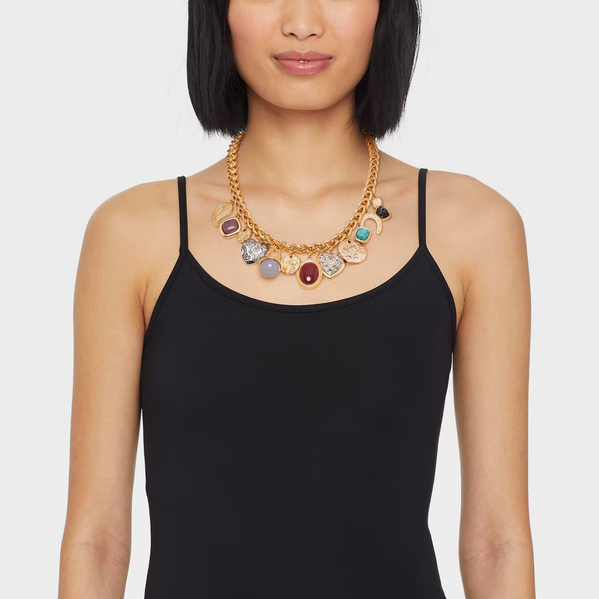 Woman wearing a black top and a gold necklace with colorful charms on a white background