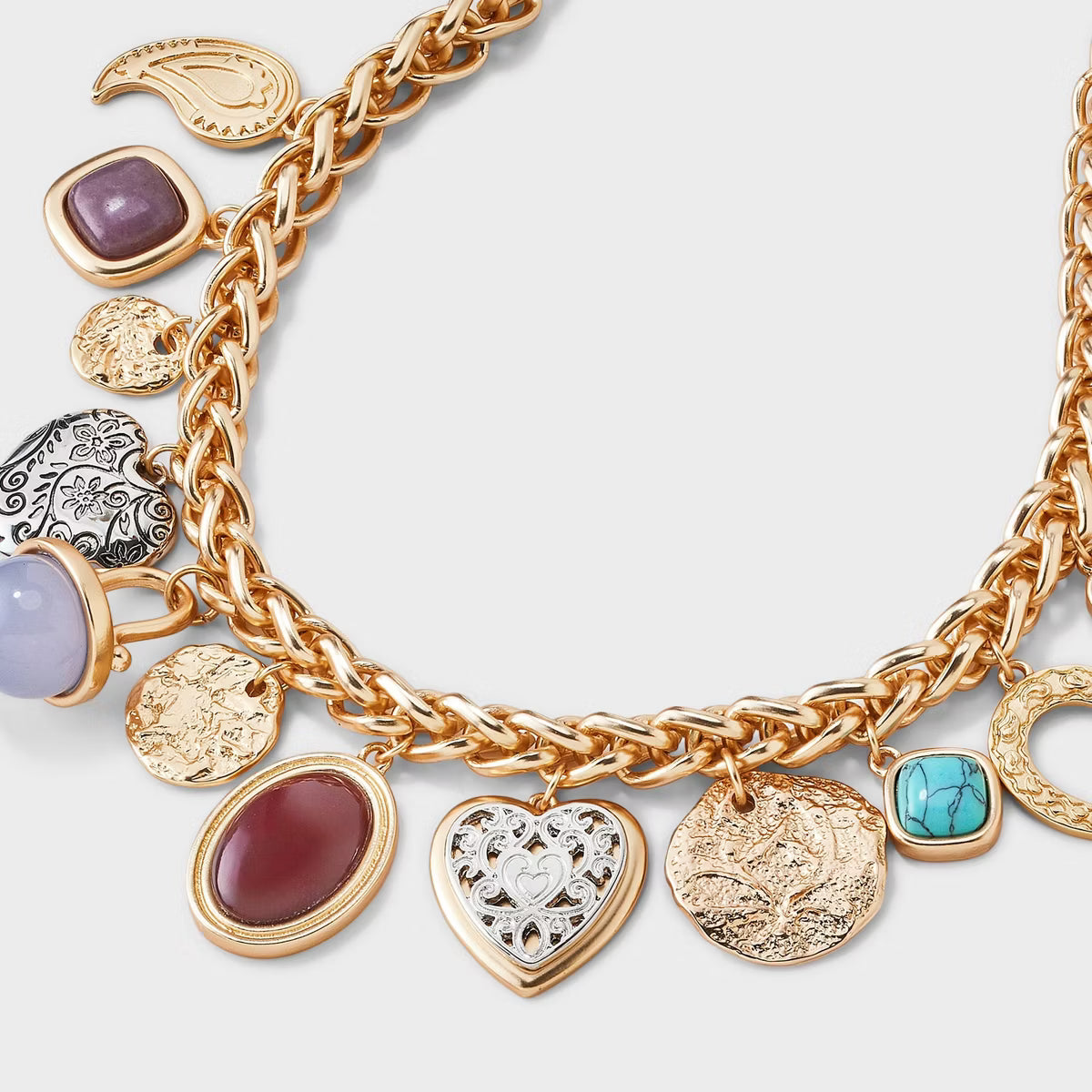 Gold charm bracelet with various charms on a light gray background