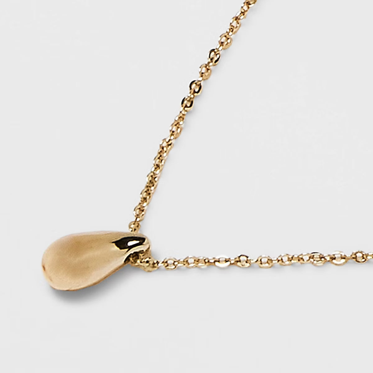Gold necklace with a teardrop-shaped pendant on a light gray background