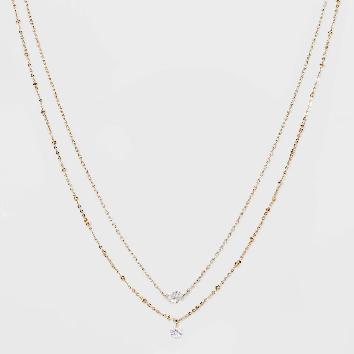 Two gold necklaces with small diamond pendants on a light gray background