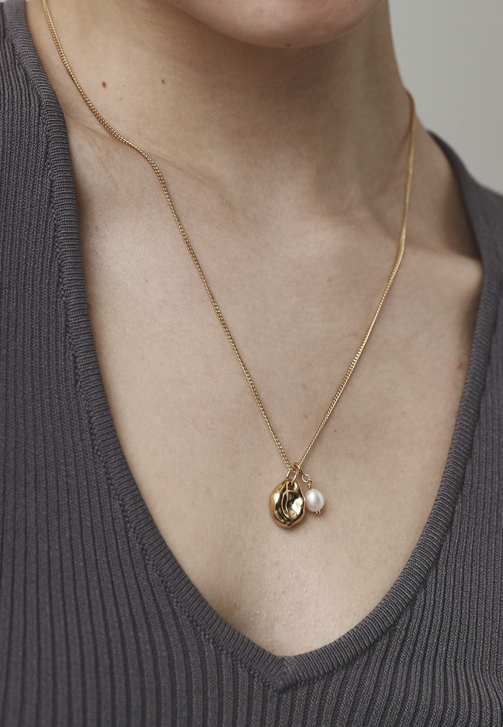 Gold necklace with a pendant on a person wearing a gray top.