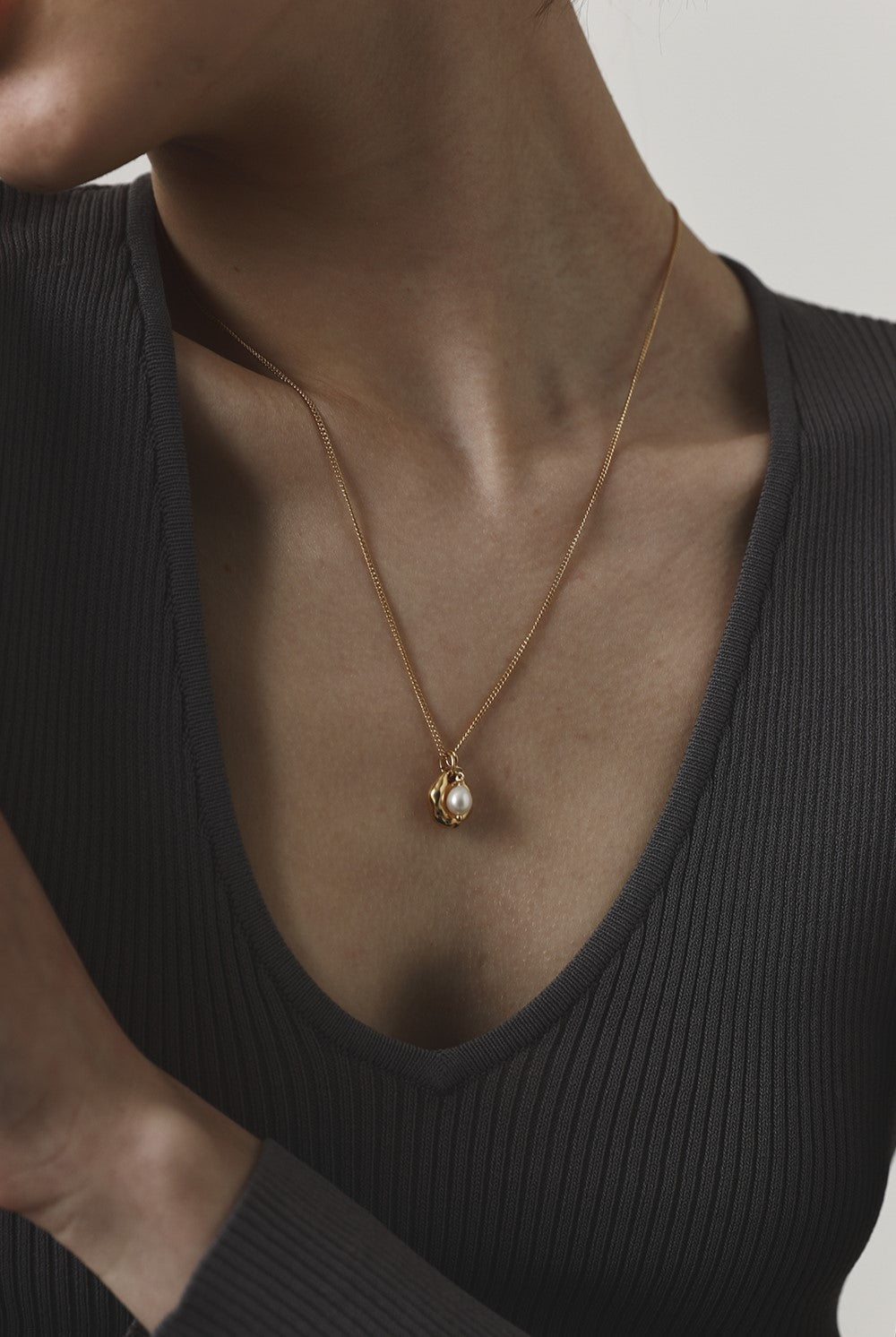 Gold necklace with a pendant worn by a person in a black top against a neutral background