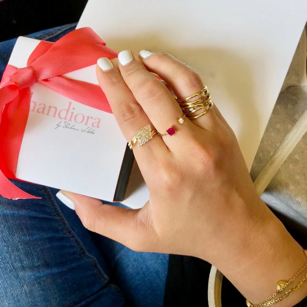 Hand with gold rings holding a gift box with 'Handiora' branding