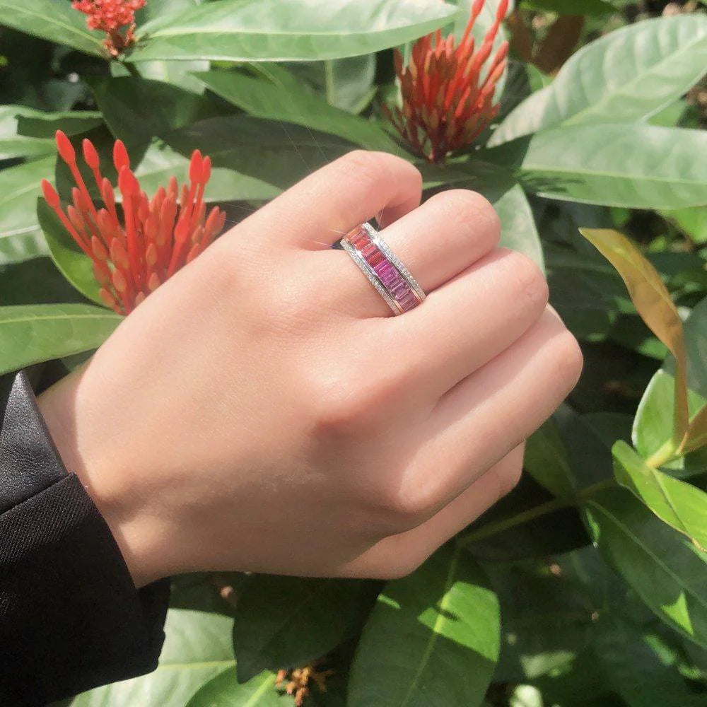 Hand wearing a ring with red flowers and green leaves in the background