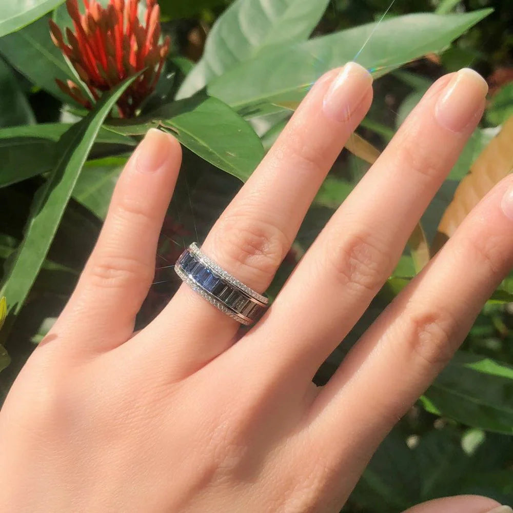 Hand wearing a ring with a blue gemstone against a green leafy background