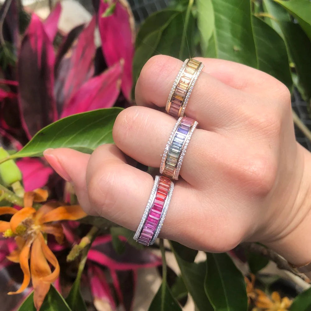 Hand wearing multiple colorful rings with a green leafy background