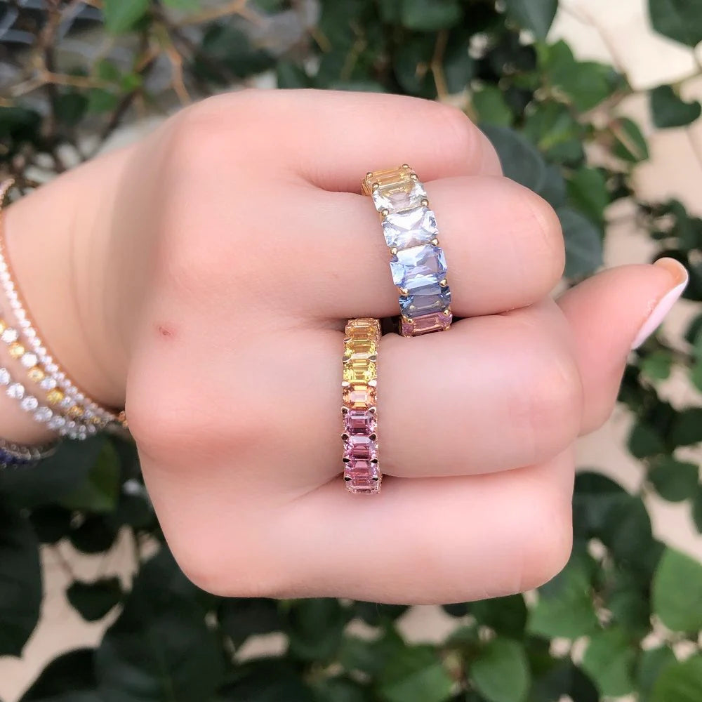 Hand wearing two colorful eternity rings with a green leafy background