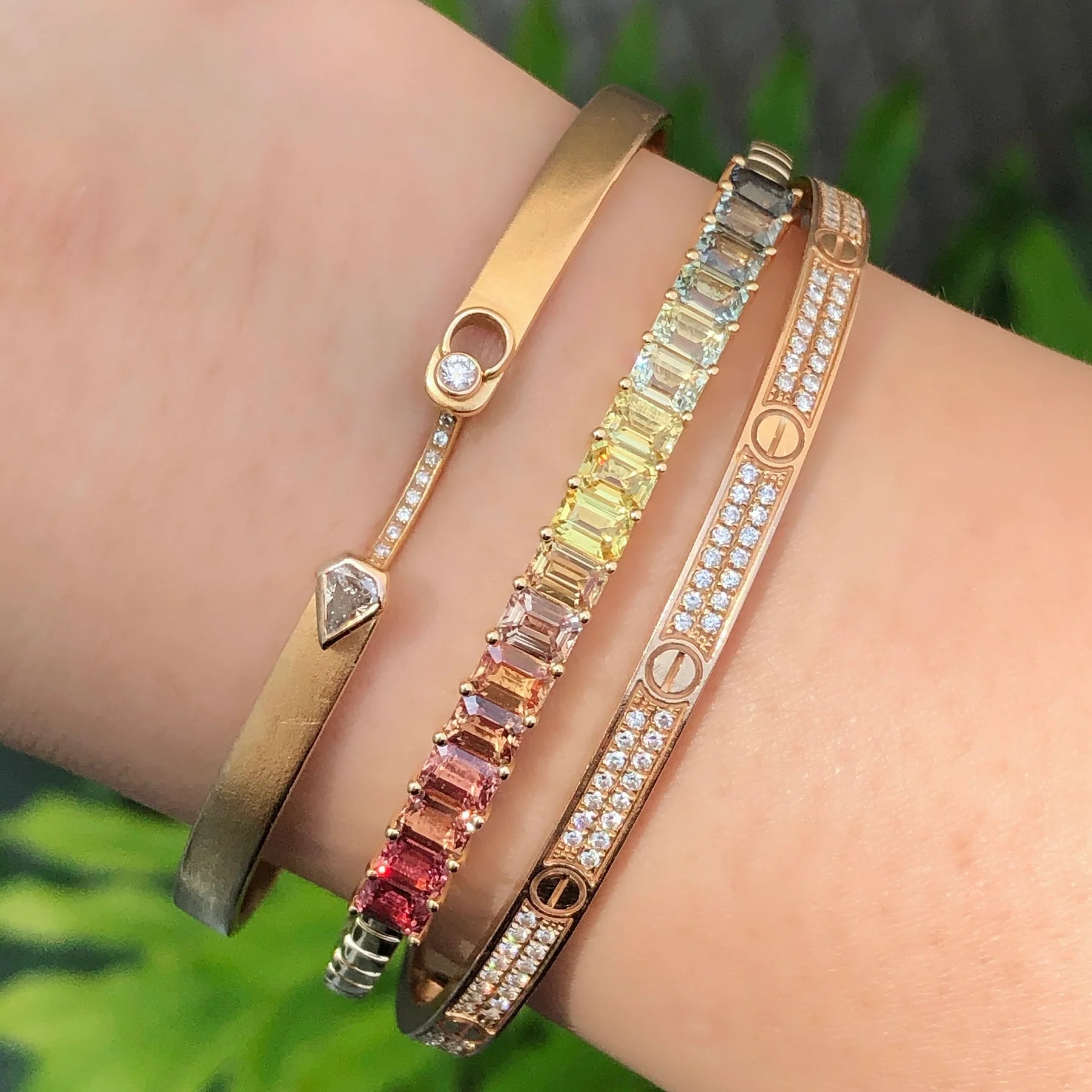 Three colorful gemstone bracelets on a wrist with a blurred green background