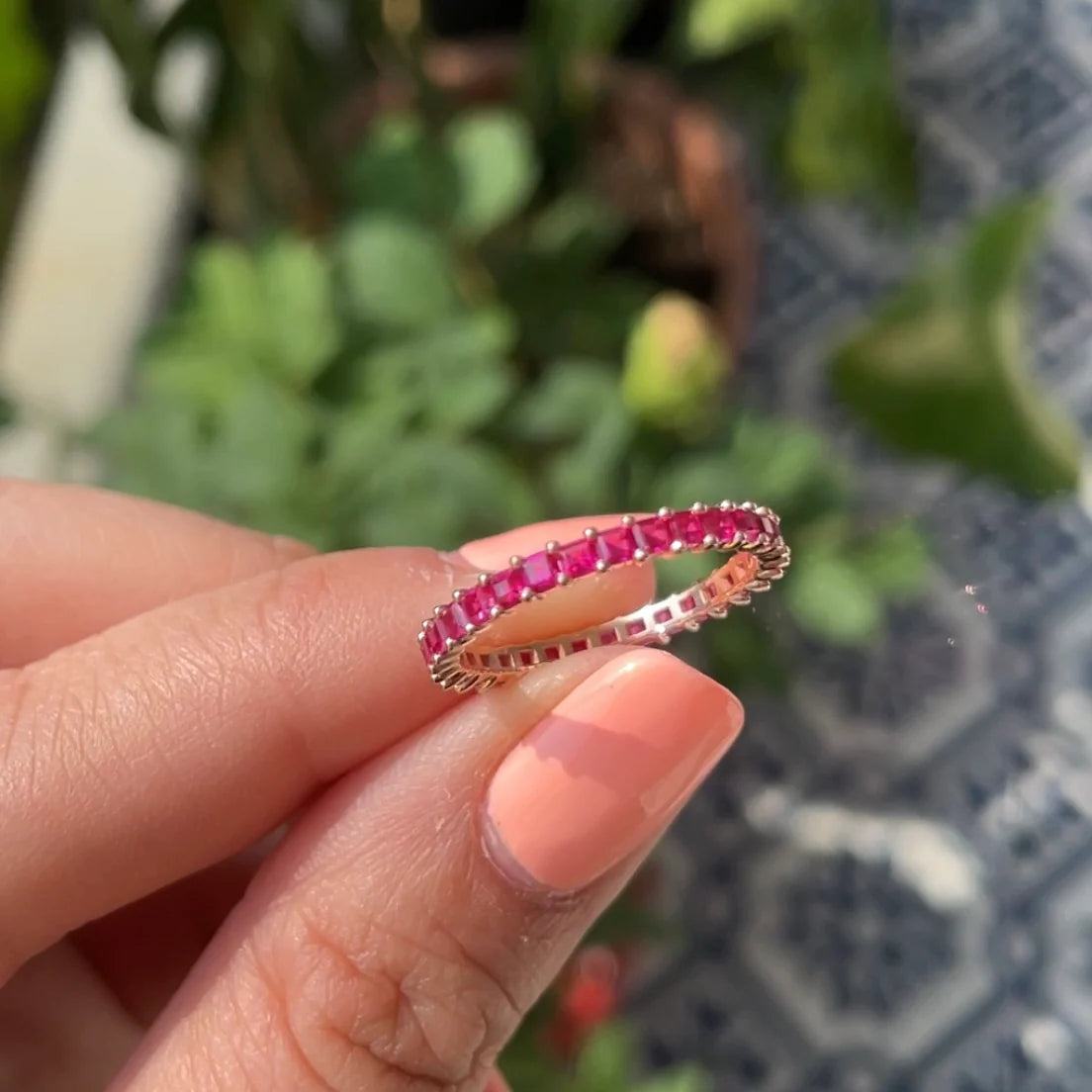 Hand holding a ring with pink gemstones against a blurred outdoor background