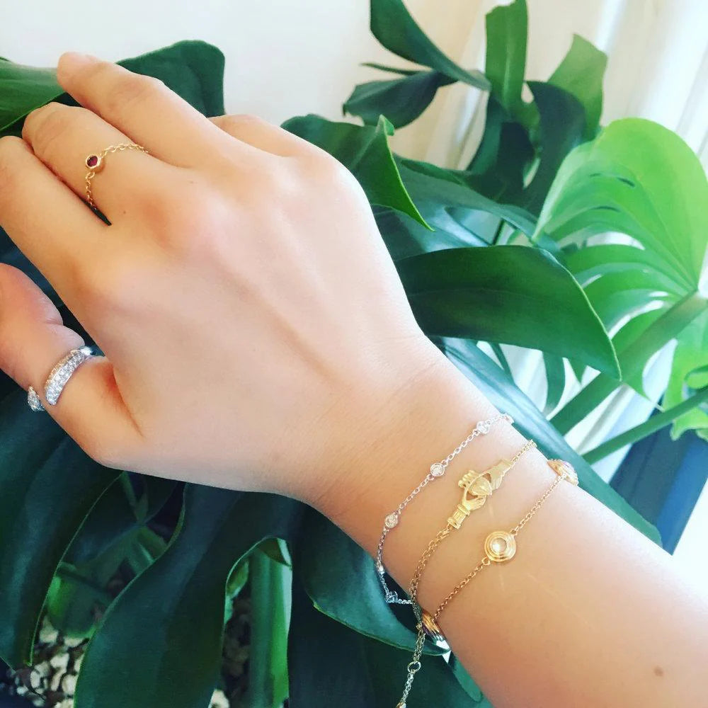 Hand wearing gold rings and bracelets with a green leafy background