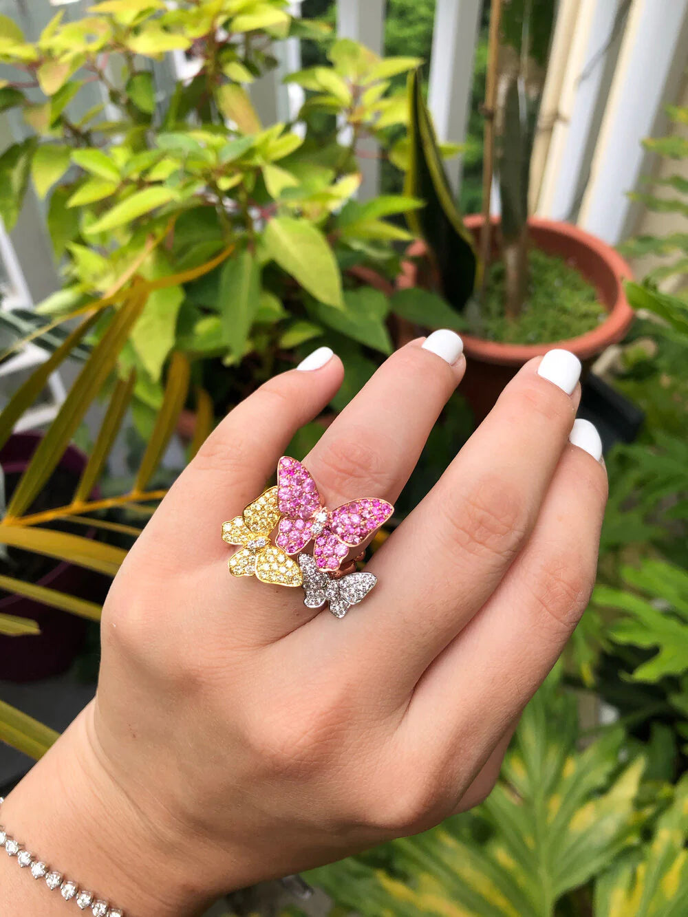 Hand wearing a colorful butterfly ring with plants in the background