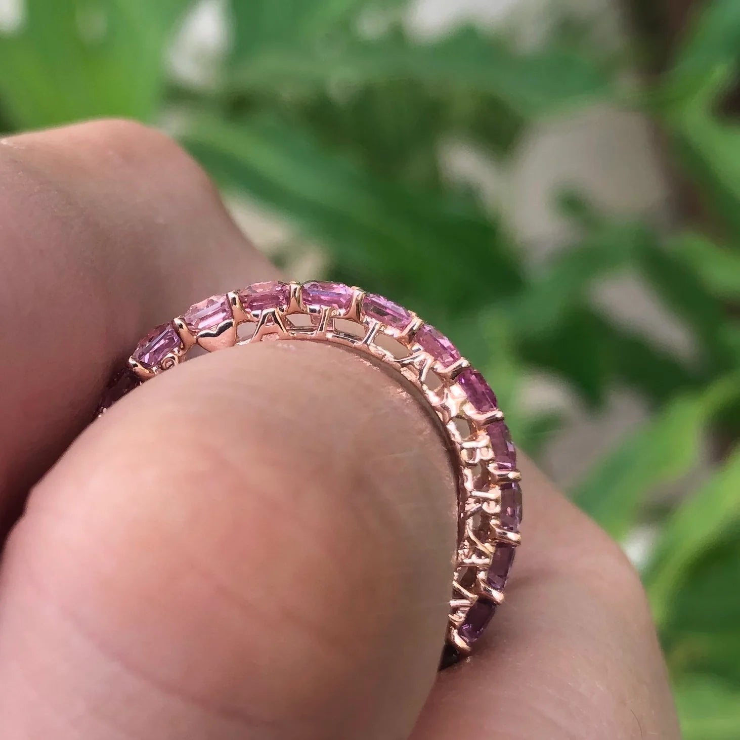 Rose gold ring with pink gemstones on a finger against a blurred green background