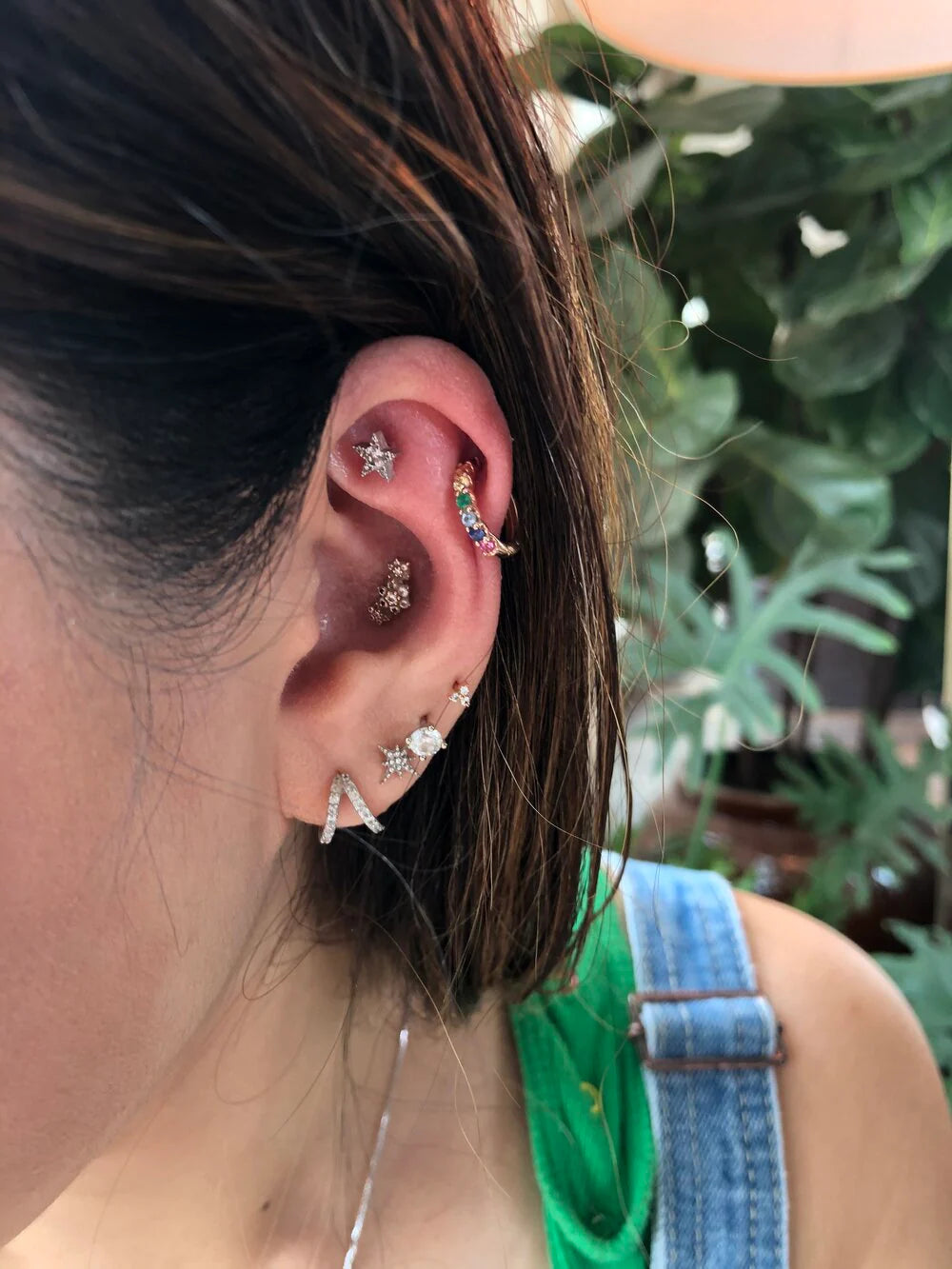 Close-up of an ear with multiple earrings against a blurred green background