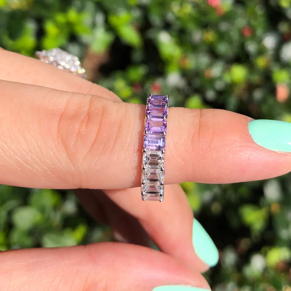 Emerald cut rainbow sapphire and diamond eternity ring on a hand