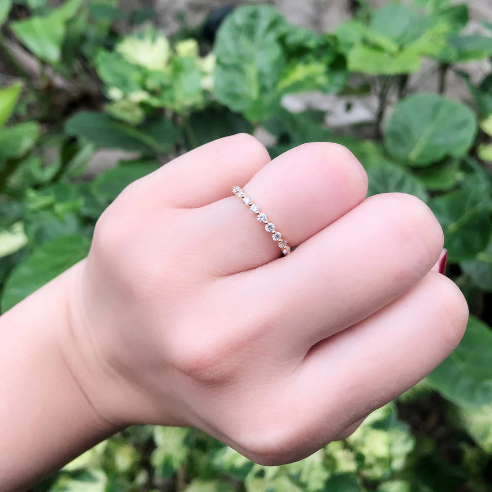 Hand wearing a delicate ring with green foliage in the background