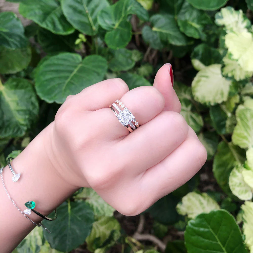 Hand wearing a diamond ring with green foliage in the background