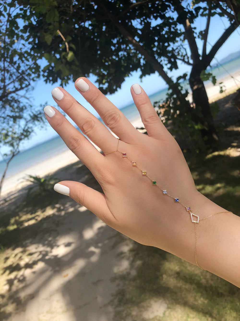 Hand with delicate gold jewelry against a blurred natural background