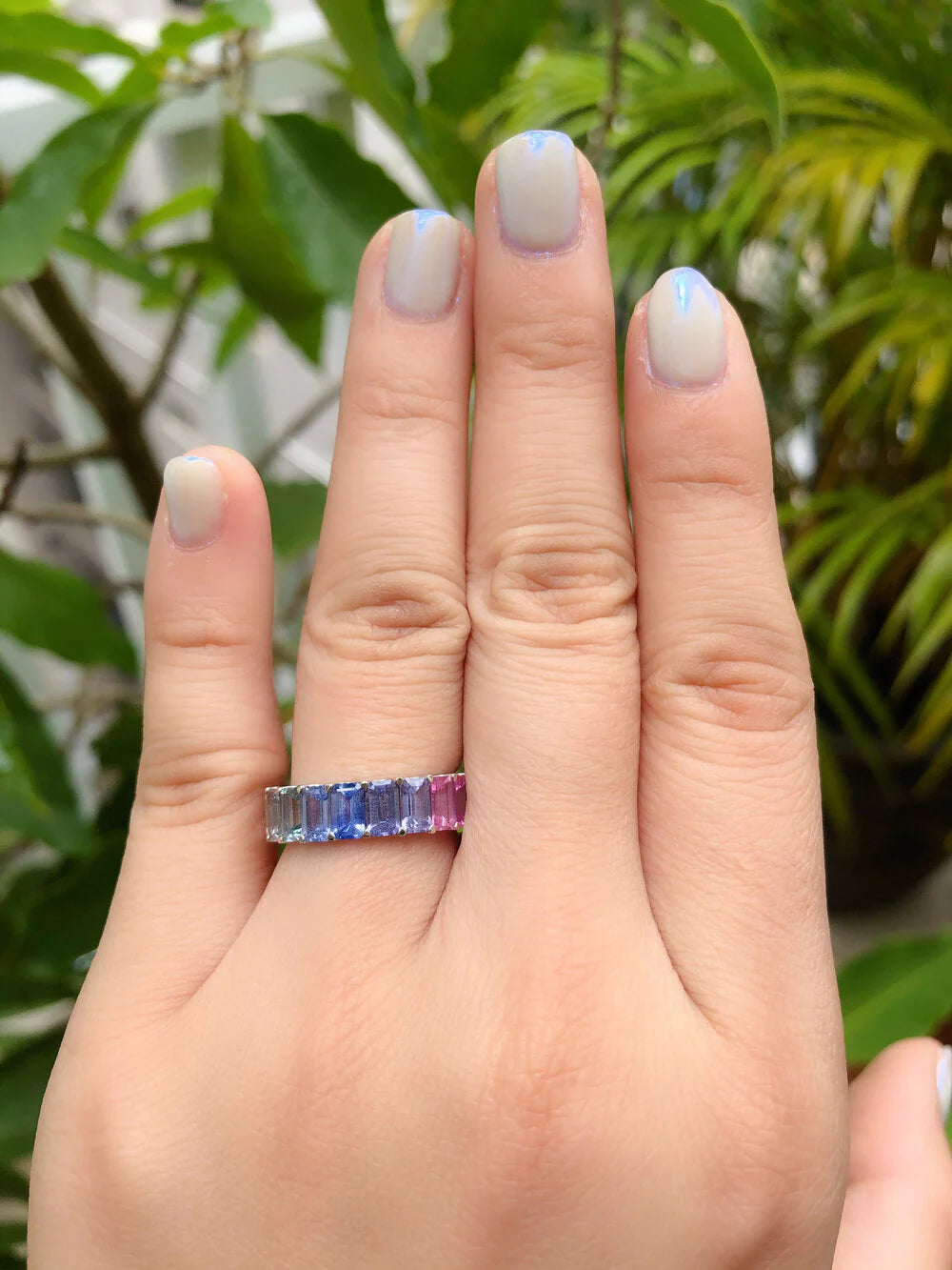 Close-up of rainbow pastel sapphires and emerald cut diamonds in eternity ring