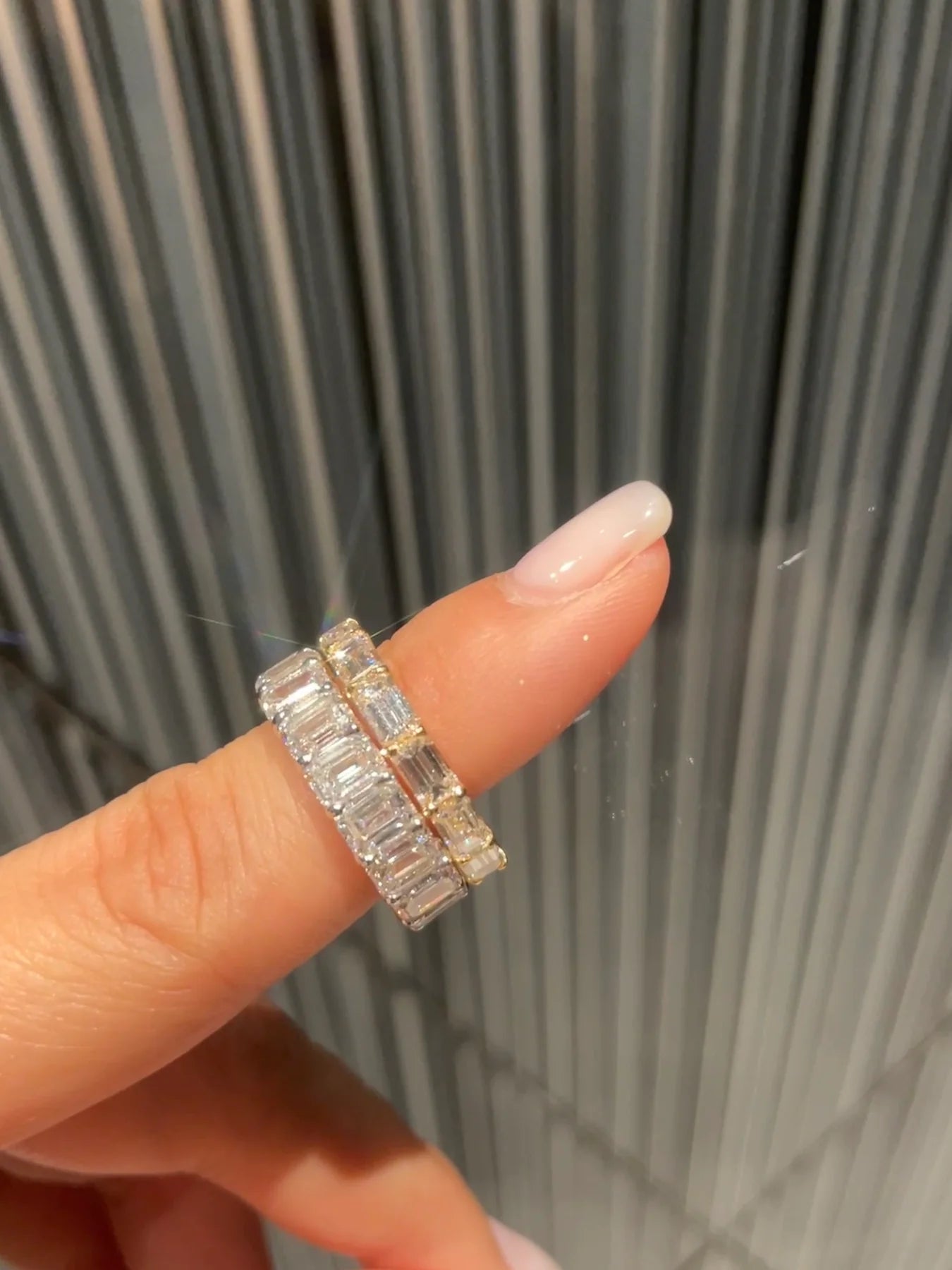 Horizontal emerald cut diamond eternity ring stacked with an engagement ring