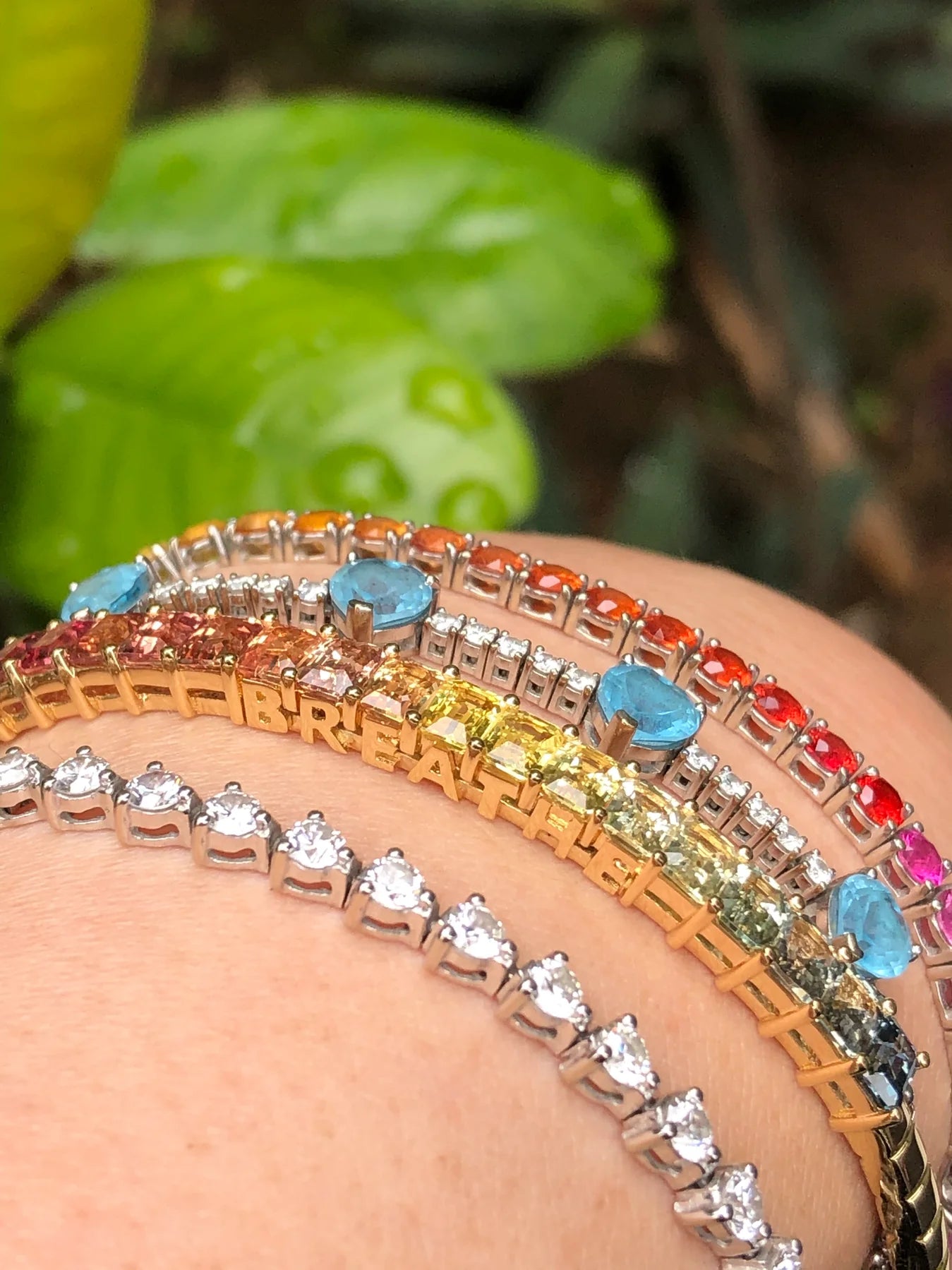 Two bracelets on a wrist with one featuring colorful gemstones and the other with clear gemstones.