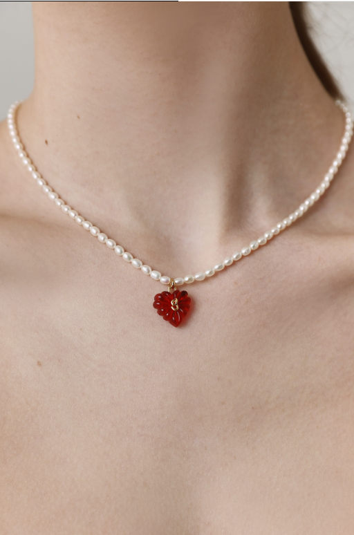 Pearl necklace with a red pendant on a neutral background