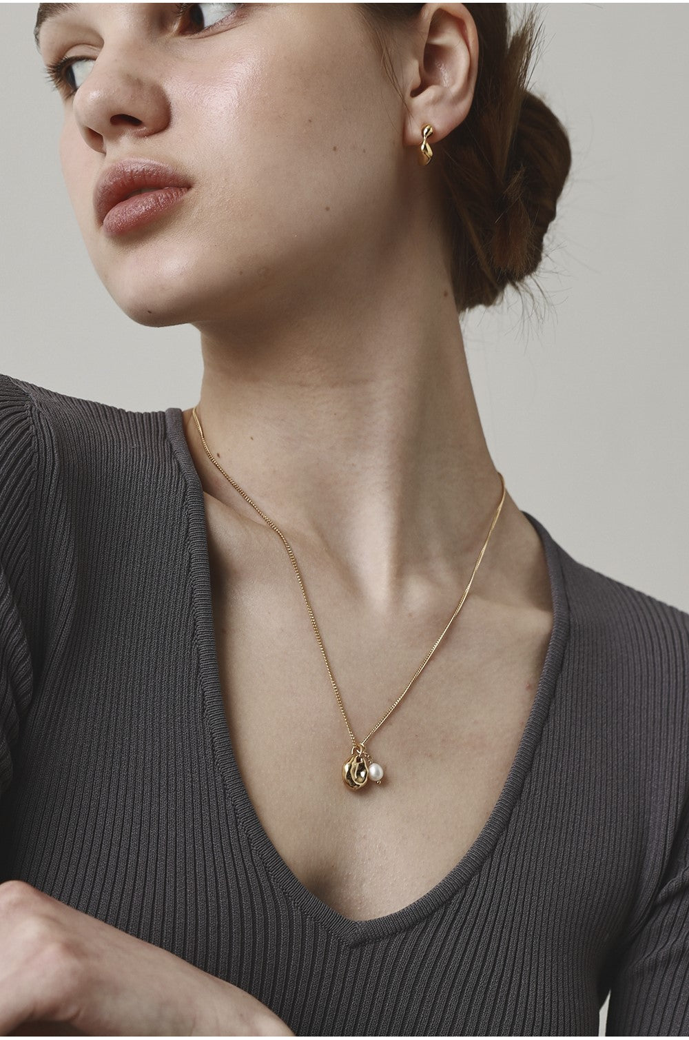 Woman wearing a gold necklace and earrings against a neutral background