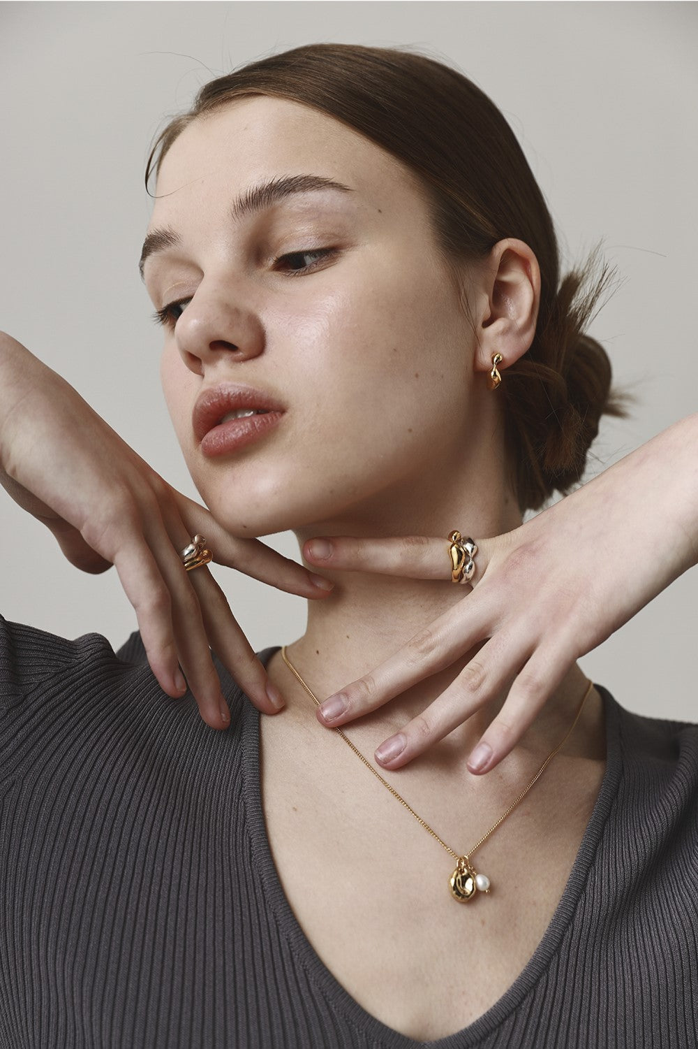 Woman wearing gold jewelry including a necklace, earrings, and ring against a neutral background