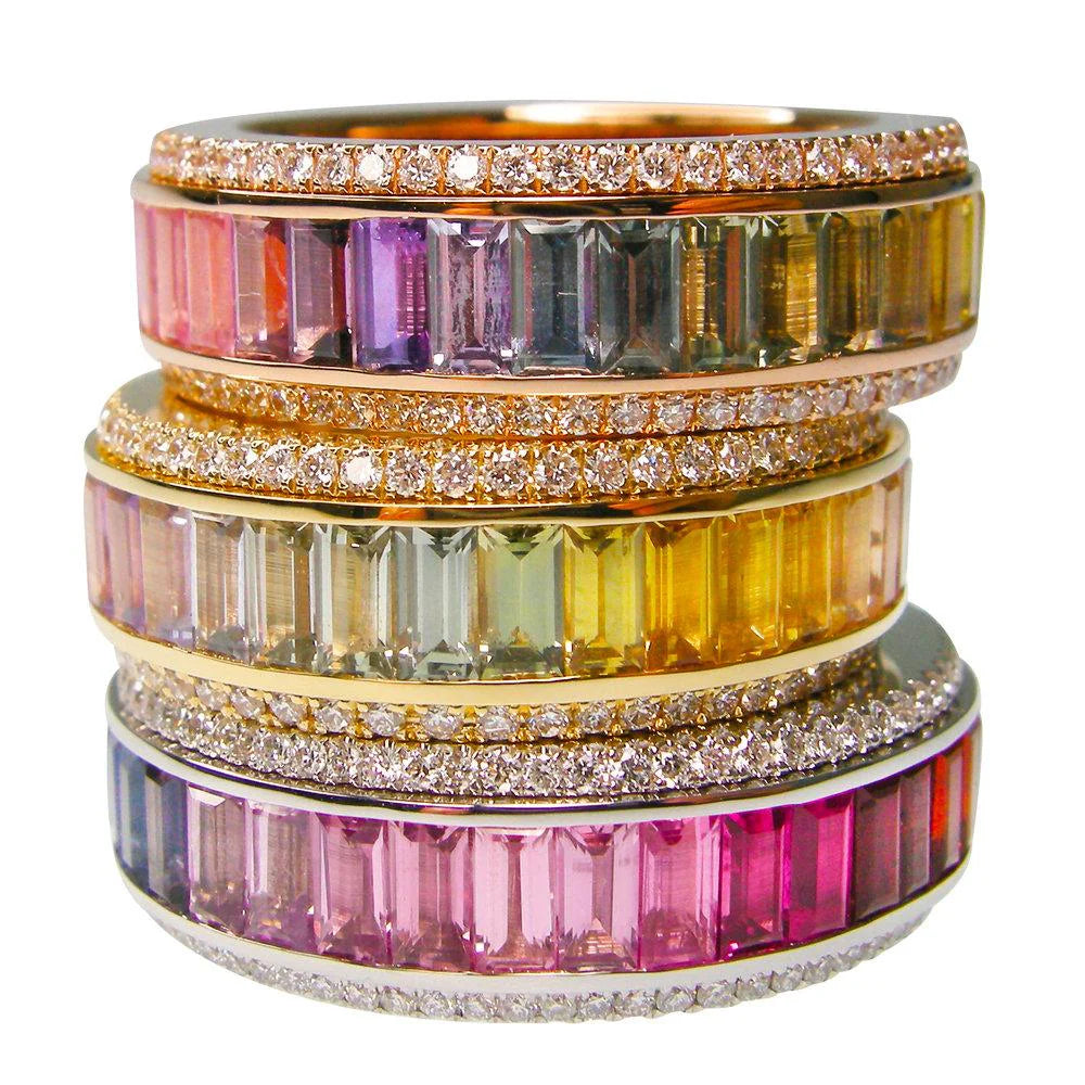 Stack of colorful gemstone rings with gold bands on a white background